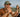 Man taking a photo of himself and a woman in a canoe on a lake with trees in the background.