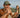 Man taking a photo of himself and a woman in a canoe on a lake with trees in the background.