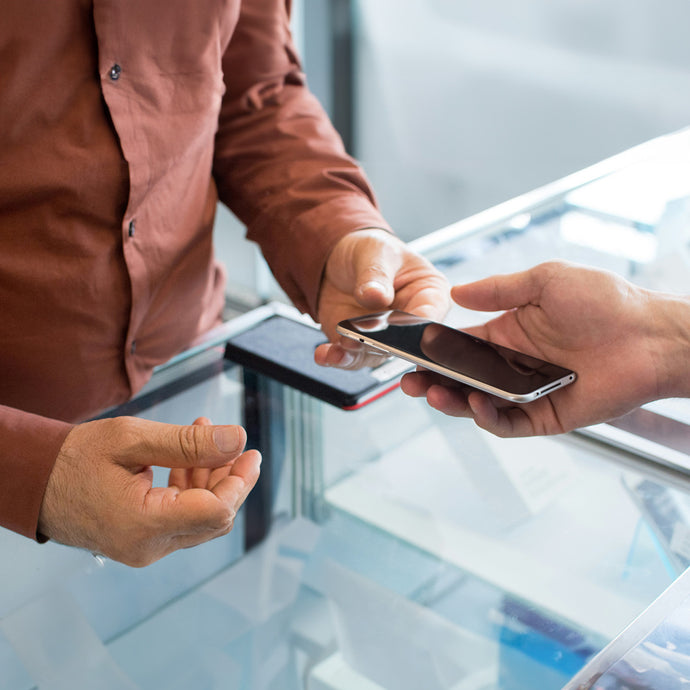 Customer handing a smartphone to a technician at a repair service counter