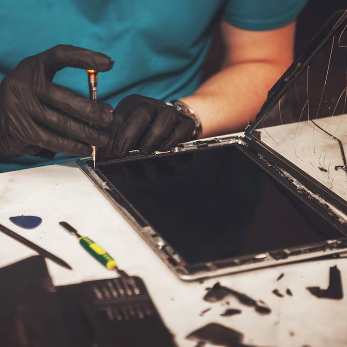 Technician wearing black gloves repairing a tablet with a screwdriver on a workbench