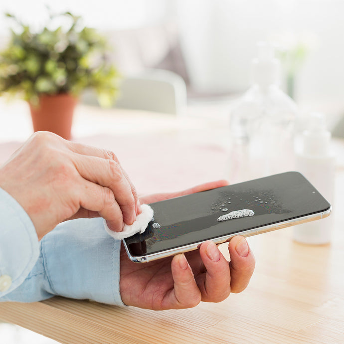 Person cleaning a smartphone screen with a cloth and cleaning solution on a wooden table