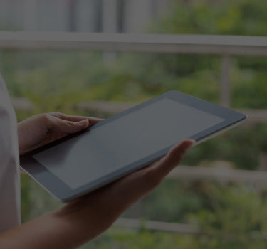 Person holding a tablet with a blurred green outdoor background