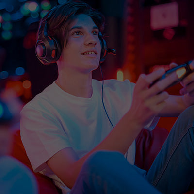 Person playing a video game with headphones on in a dark room with colorful lights.