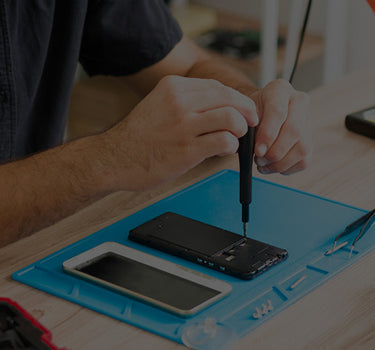 Person repairing a smartphone on a blue mat with tools and parts.