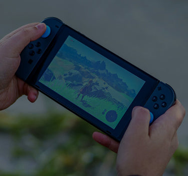 Person holding a gaming console with a game displayed on the screen against a blurred natural background