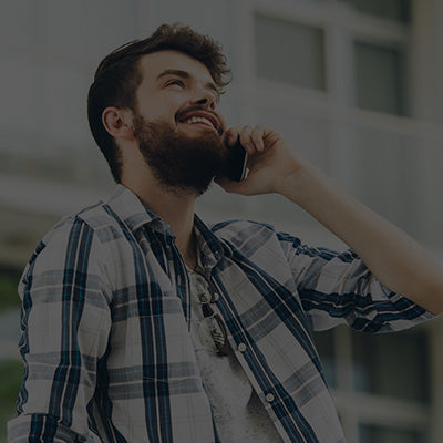 Man with a beard talking on a phone outdoors