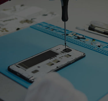 Person repairing a smartphone with tools on a blue mat