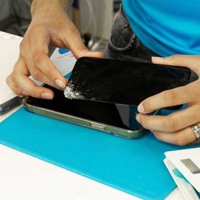 Technician holding a smartphone with a cracked screen on a blue surface