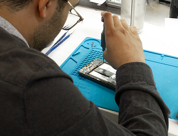 A technician fixing a cell phone on a table with precision tools