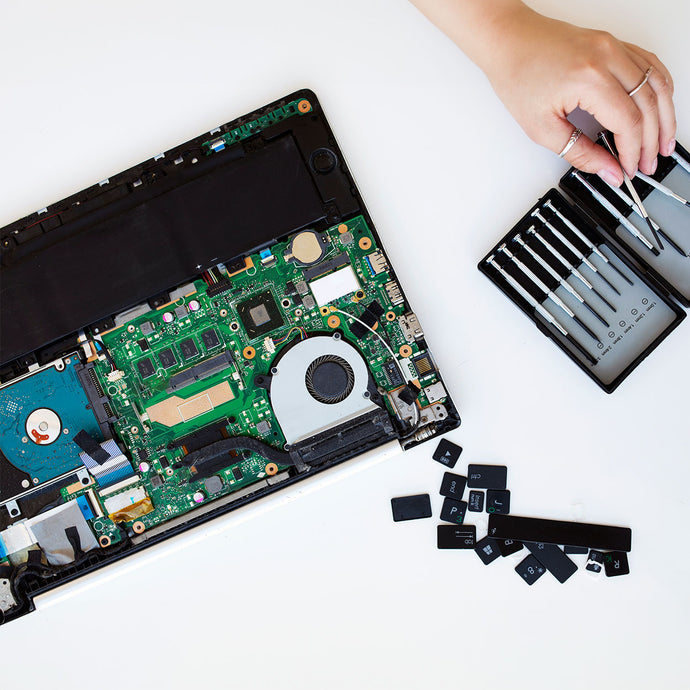 Laptop with open casing, circuit board exposed, and tools on a white background