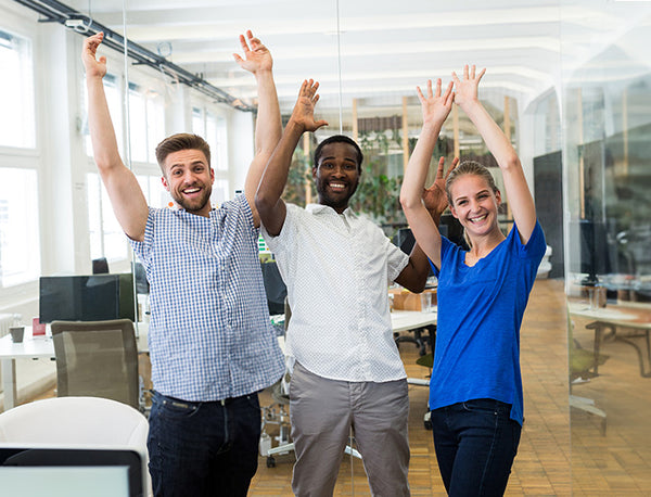Three smiling people with their arms raised; two men and one woman