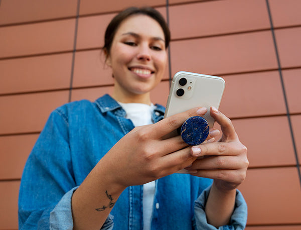 A woman wearing a blue jacket, smiling while holding and looking at her white cell phone