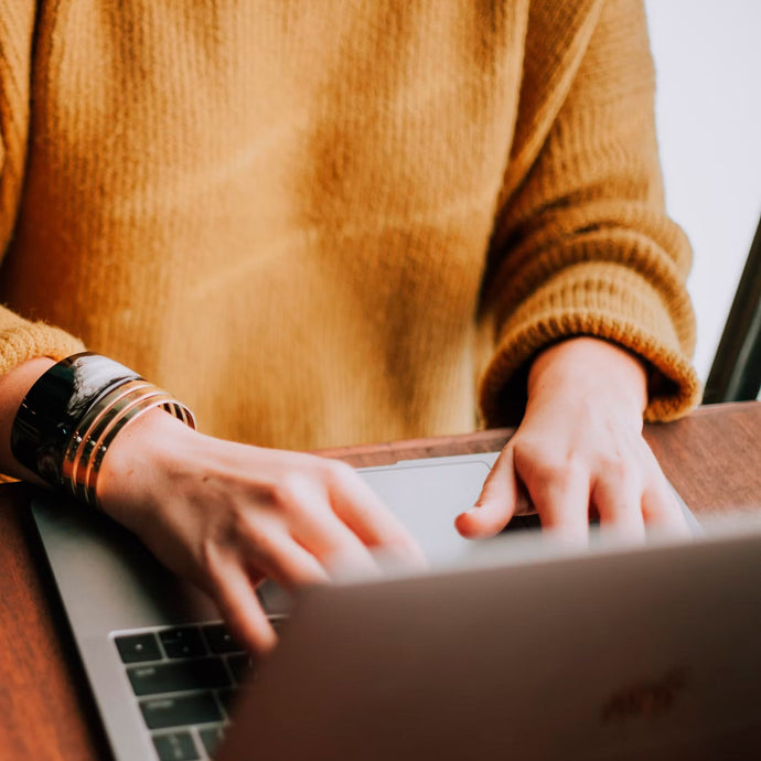 Person typing on laptop wearing mustard-colored sweater