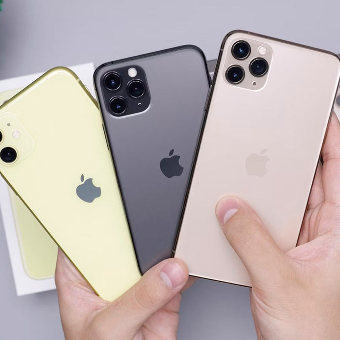 Hand holding three iPhones in different colors with rear cameras visible
